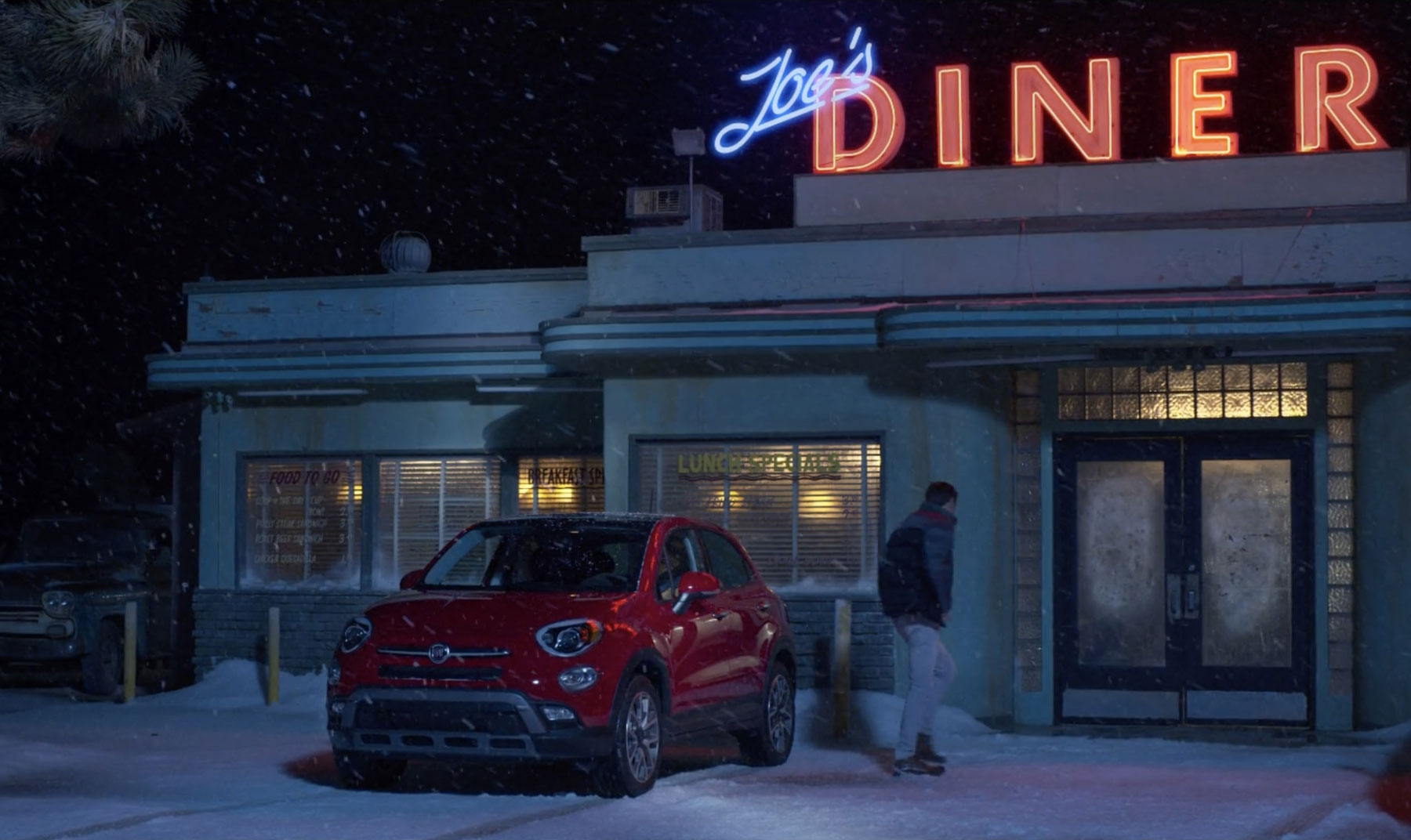 A red Fiat outside a snow-covered diner at night